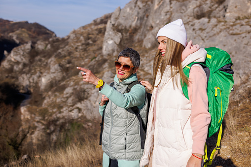 Mature mother and young adult daughter standing and admiring the view while hiking in rocky mountains