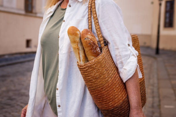 Woman with baguette bread in reusable straw bag Woman with baguette bread in straw bag. Sustainable lifestyle and reusable shopping bag straw bag stock pictures, royalty-free photos & images
