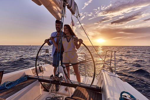 Young happy couple enjoying while driving a yacht in summer sunset at sea. Copy space.