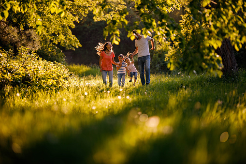 Happy family having fun while holding hands and running during spring day in nature. Copy space.
