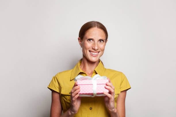 istock Attractive optimistic happy smiling woman with pink gift present box with white ribbon against white studio wall  banner background 1461558817
