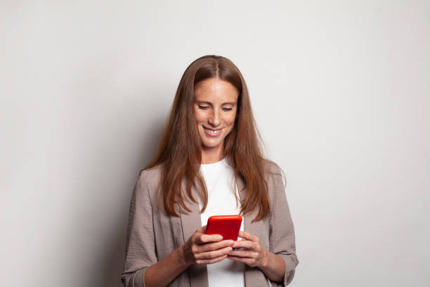istock Optimistic happy smiling woman using smart phone against white studio wall banner background 1461558846