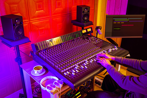 male professional sound engineer, music producer hands working on audio mixing console in home studio