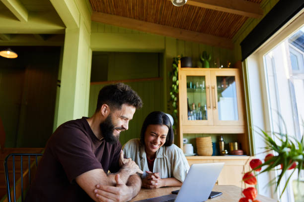 istock Couple laughing at something on a laptop while sitting in their kitchen 1461560660