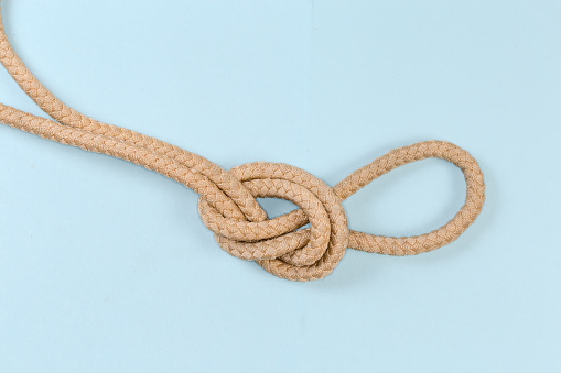 Rope knot Overhand loop, also known as loop knot tied with a climbing rope, close-up on a blue background