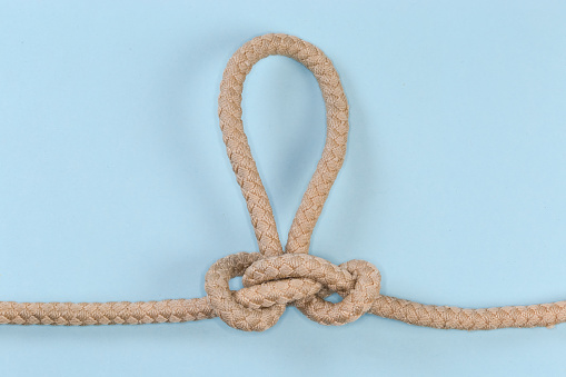 Rope knot Butterfly loop, also known as Swiss loop tied with a climbing rope on a blue background