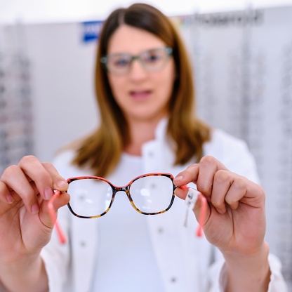 Woman at optician holding eyeglasses she want to buy. Selective focus on glasses.