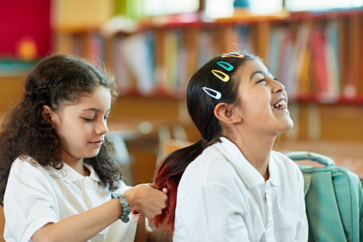 Waist-up view of 9 year old Hispanic students in school uniforms taking a break for hair care.