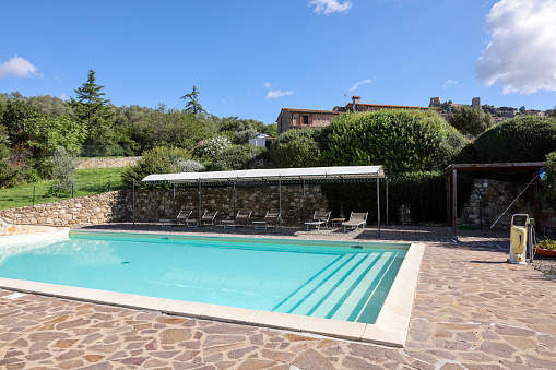 An outdoor pool with people resting on chairs on a side in the back of a villa - rural houses for rent