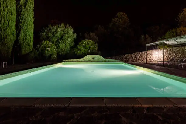 Photo of Illuminated swimming pool on the Montemassi hillside surrounded by cypresses and oleanders. Italy
