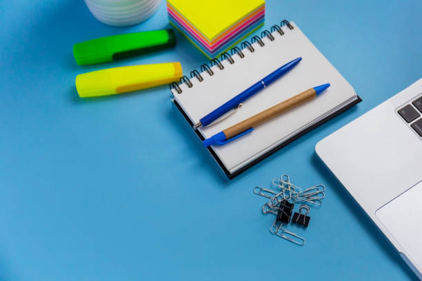 istock Flat lay workspace with a laptop, a notepad, and two pens, on blue background 1461570268