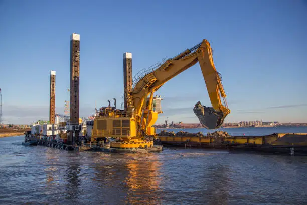 In the port, a large floating dredging excavator scoops up soil from the bottom