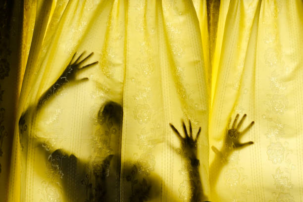 A person stands with arms raised to pull back burgundy curtains, revealing daylight at a bright window. Wearing a yellow hoodie with a heart motif on the back, the scene feels warm and hopeful.