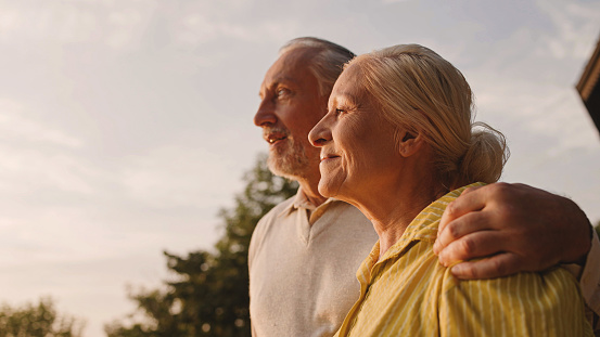 Smiling aged couple hugging outdoors, enjoying city view at sunset, family love