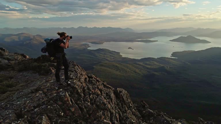 Young man taking a photo of a grand mountain landscape scene at sunset in the wilderness of Tasmania