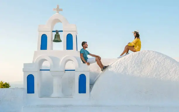 Young couple of men and women tourists visit Oia Santorini Greece on a sunny day during summer with whitewashed homes and churches, Greek Island Aegean Cyclades