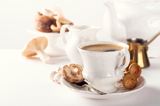Trendy mushroom coffee in white porcelain vintage cup over white background. New Superfood Trend. Copy space, selective focus.