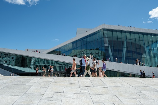 Oslo, Norway – July 07, 2022: A low angle shot of people walking along the modern Opera building in Oslo, Norway