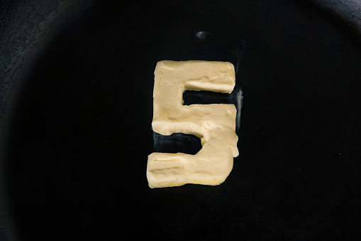 A closeup shot of a piece of butter in the shape of number 5 on a hot pan