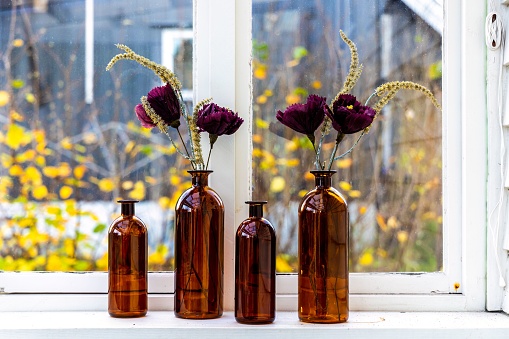 A set of brown decorative bottles serving as vases for beautiful artificial flowers set by the window