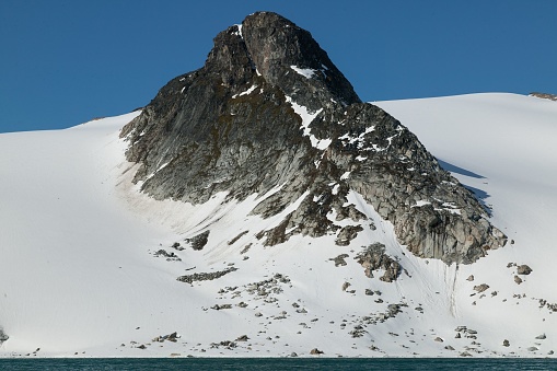 A big snowy mountains with huge rocky peaks in Svalbard against the blue sky