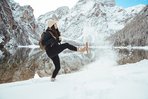 Woman with backpack kicking snow on the winter background