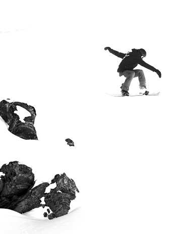A vertical shot of a snowboarder jumping off a cliff