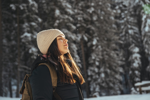 Young woman standing on snow covered forest with eyes closed