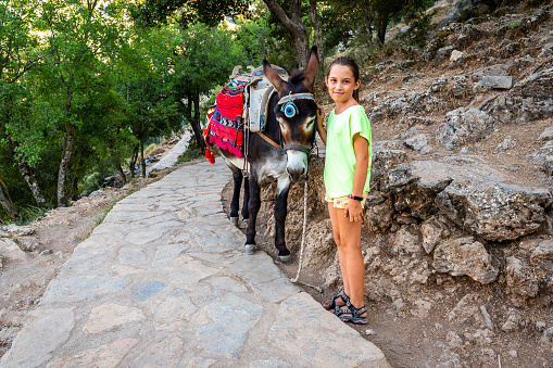 Girl riding a donkey to visit Cave of Diktaion Andron. Tourists visitingfamous cave Diktaion Andron, the birthplace of god Zeus in Lasithi plateau,Crete, Greece with a traditional donkey.