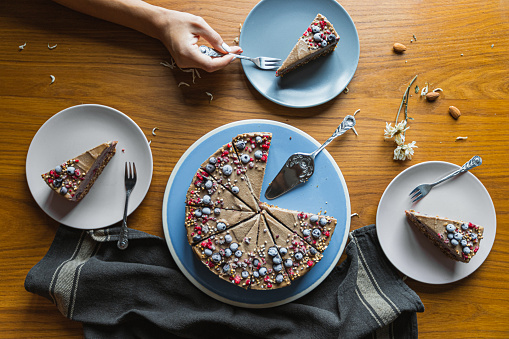 A top view of a person eating a piece of delicious creamy cake with berries on the table