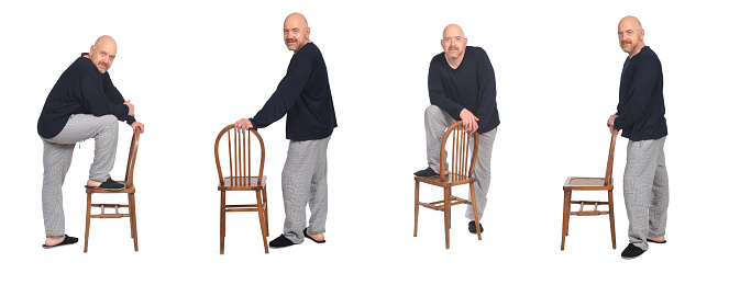 group of same man with pajamas standing and playing with chair on white background