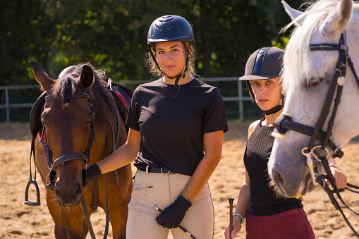 Two young Caucasian girl riders having fun with their white and brown horses on a horse riding