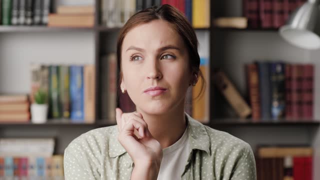 Pensive woman, brainstorming, good idea concept. Concentrated woman in office or apartment pensively holds her chin with her hand, inspiration comes and she with smile looking at camera. Headshot
