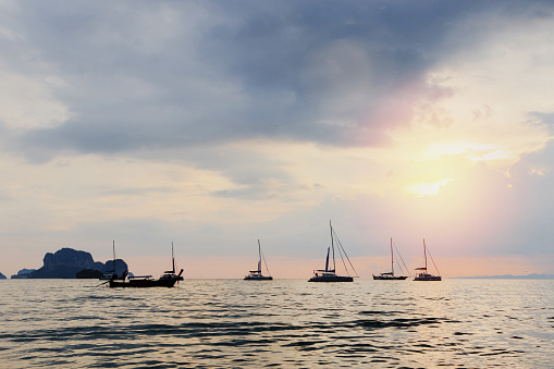 Serene sea with silhouettes of various boats against a sunset sky
