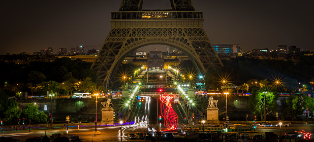 Eiffel Tower in the evening without lighting, carousel with plenty of light bulbs and lighting in forefront, view from low angle, cloudy sky in the background, horizontal