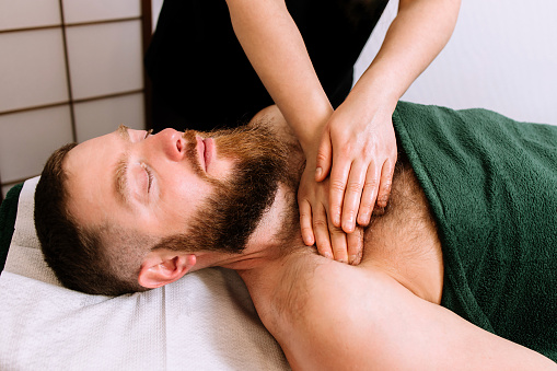 Bearded man receiving complex facial and chest massage in beauty salon.Beauty and skincare concept with a man. Middle aged male relaxed with massage for facial lifting