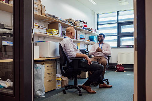 Two teachers sitting in an office together in the school that they work at in Gateshead, North East England. They are discussing lesson plans while laughing.