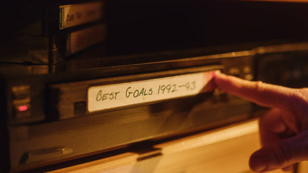 istock Retro Nineties Technology Concept. Close Up of a Person Inserting a VHS Cassette in a Player with Nostalgic Best Sport Goals Footage from World Cup. Old VCR Shot with Shallow Depth of Field and Bokeh. 1461604013