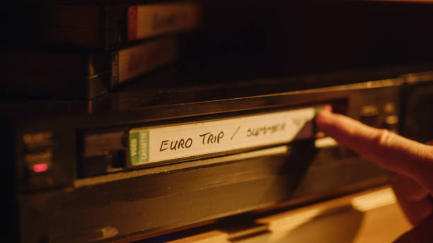 istock Retro Nineties Technology Concept. Close Up of a Person Inserting a VHS Cassette in a Player with Nostalgic Eurotrip Footage from Home Video Camera. Old VCR with Shallow Depth of Field and Bokeh. 1461604024