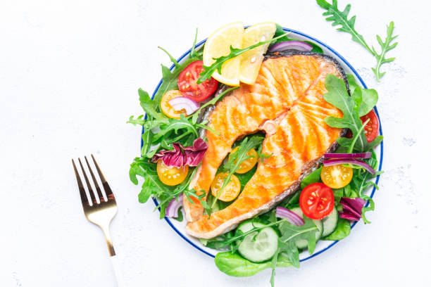 istock Grilled salmon steak with vegetables, tomatoes, arugula and lettuce side dish salad on plate, gourmet lunch. White table background, top view 1461604357
