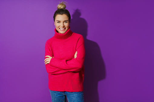 Portrait of young woman wearing warm and cozy polo neck sweater against purple background