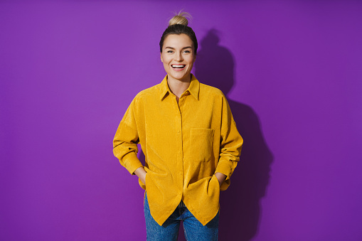 Portrait of young cheerful laughing girl wearing yellow shirt against purple background