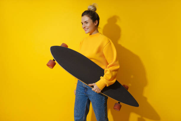 istock Young cheerful girl with longboard against yellow background 1461607355