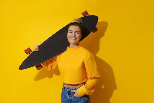 istock Young cheerful girl with longboard against yellow background 1461607723
