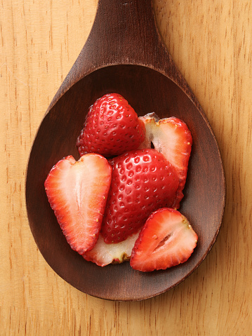 Top view of wooden spoon with halved strawberries on it