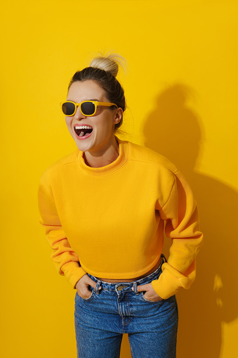 Portrait of young cheerful girl wearing yellow sweatshirt and sunglasses against yellow background