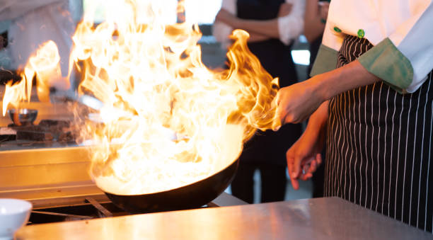 chefs that specialize in cooking will be meticulous with every cooking process. even minor details will not be overlooked. as with stir-fry, high heat will be used until a flaming flame appears - chef trainee cooking teenager imagens e fotografias de stock