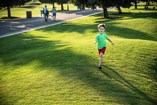 Little boy running on the grass on huge golf field.