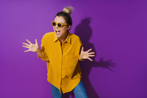 Portrait of young cheerful girl wearing yellow shirt and sunglasses against purple background