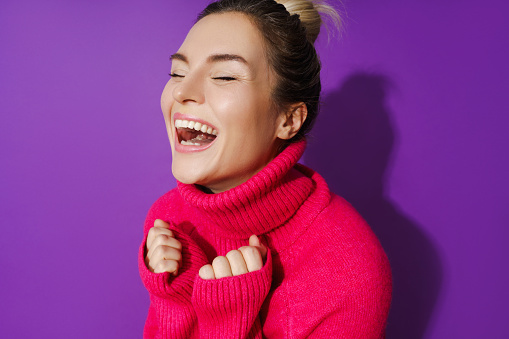 Wide-angle closeup portrait of cheerful woman wearing warm polo neck sweater against purple background